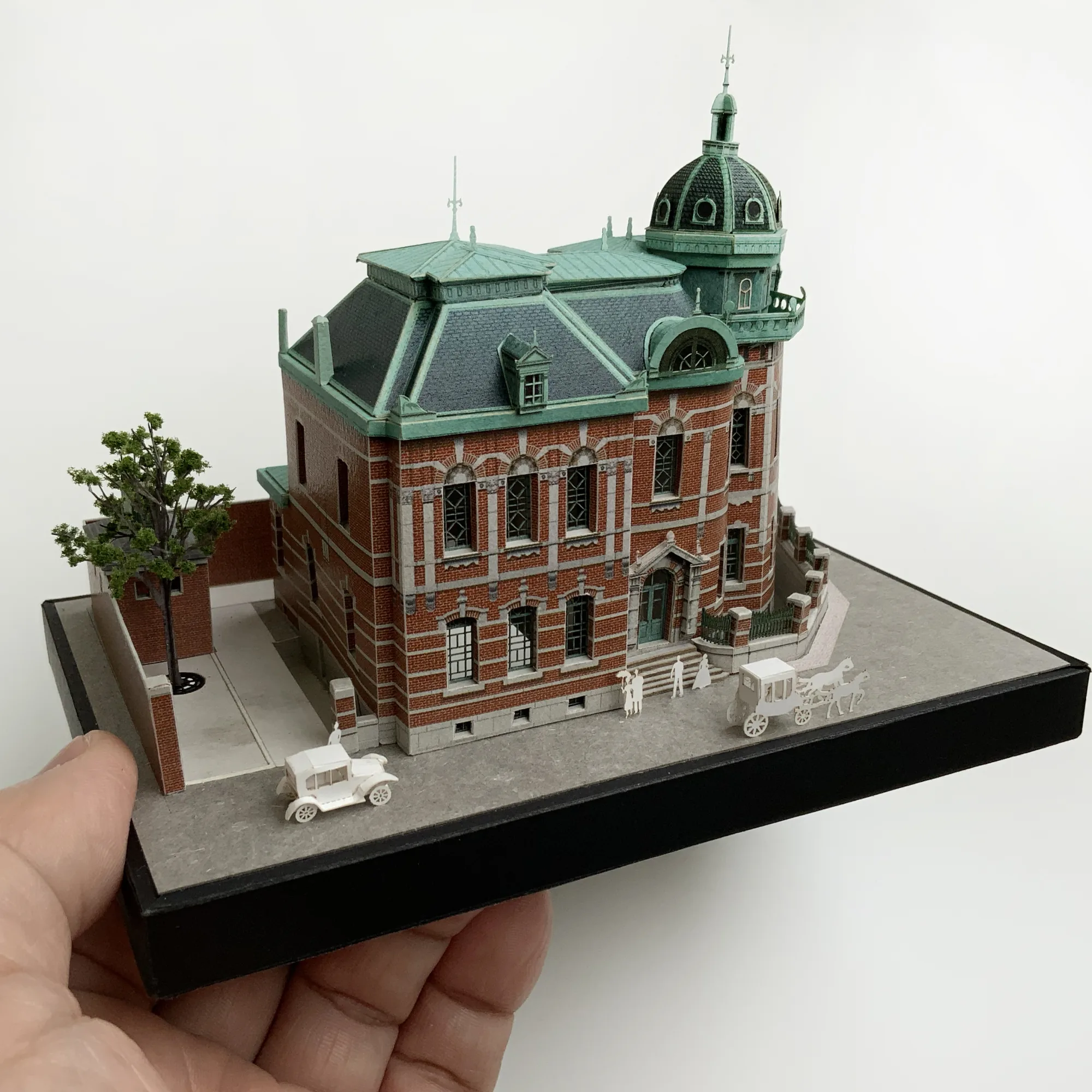 手のひらに載せた赤煉瓦文化館のペーパークラフト建築模型。緑青色のドームと煉瓦壁を再現した手のひらサイズの情景模型