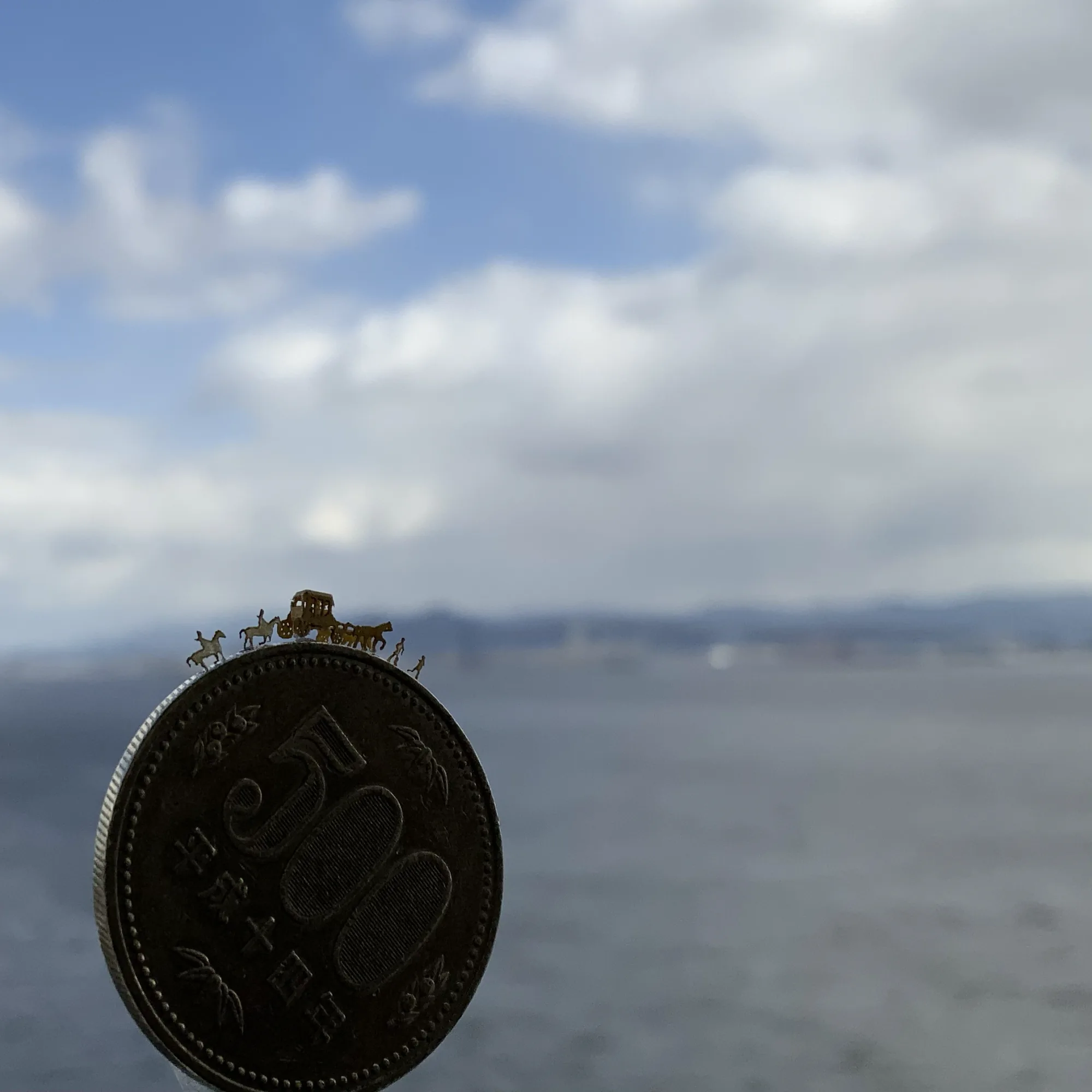 500円硬貨の上に載る極小ペーパークラフト。海を背景に撮影した、数ミリ単位で作り込んだ精密模型